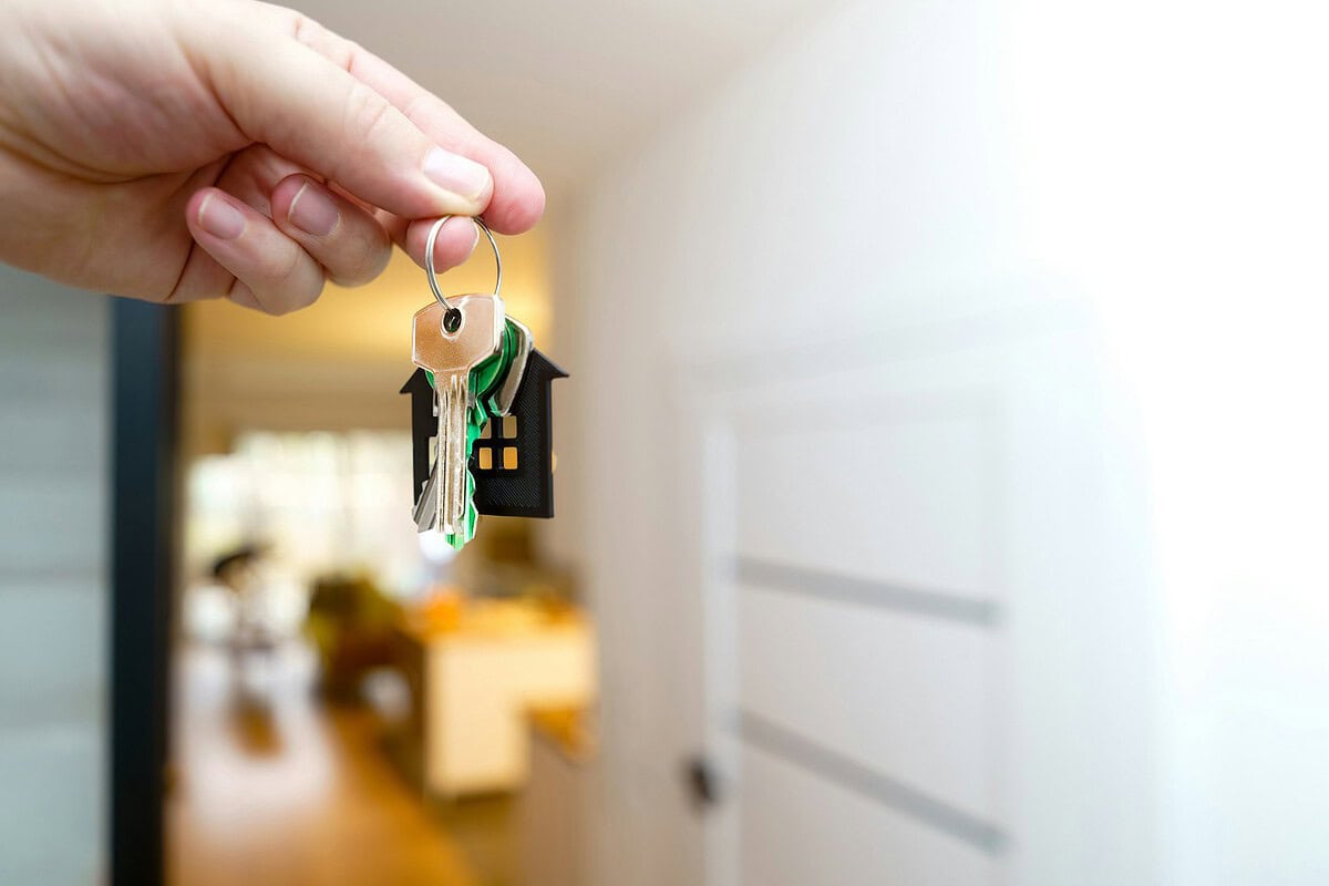 Hand met huissleutels voor de voordeur van een verhuurde woning, geregeld met een verhuurdersverzekering