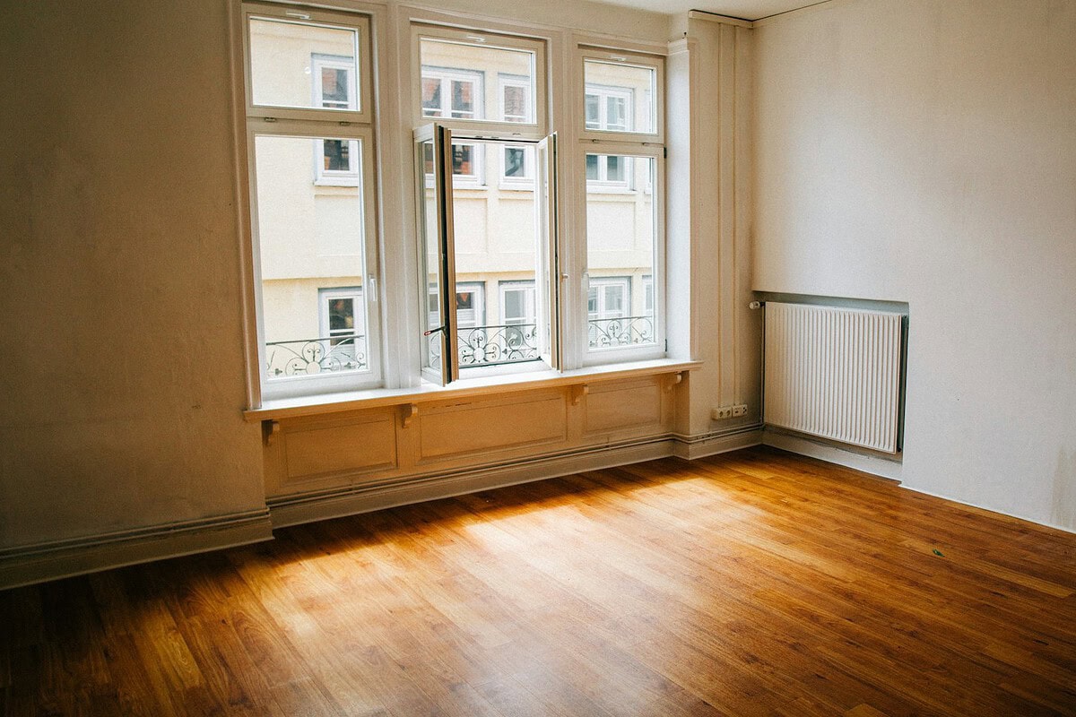 Lege kamer met houten vloer en groot raam in een leegstaand pand